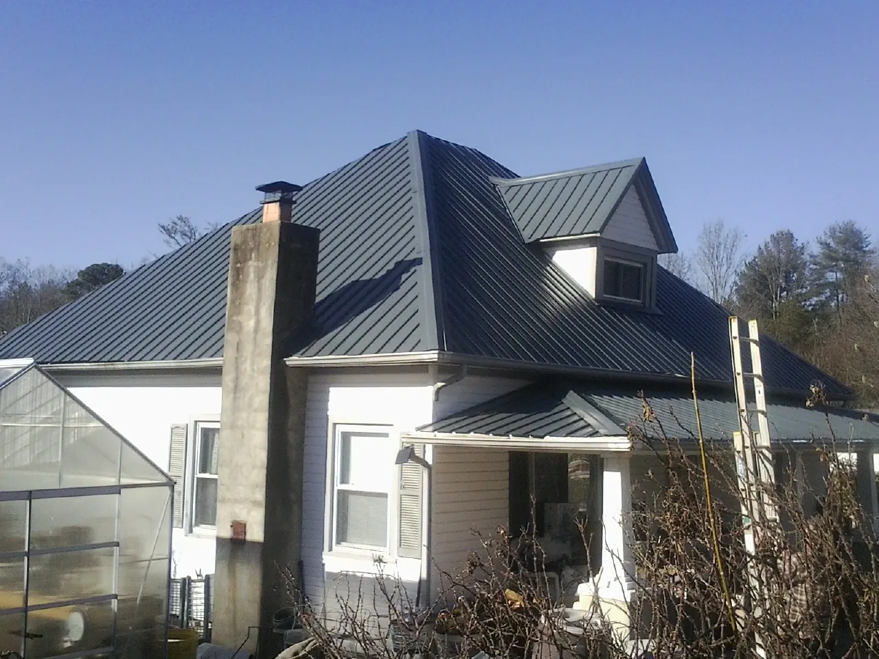 Dark blue standing seam metal roof on a white farmhouse with dormer — Slate & Tile Roof Repair by Roofing Brothers in Lefor