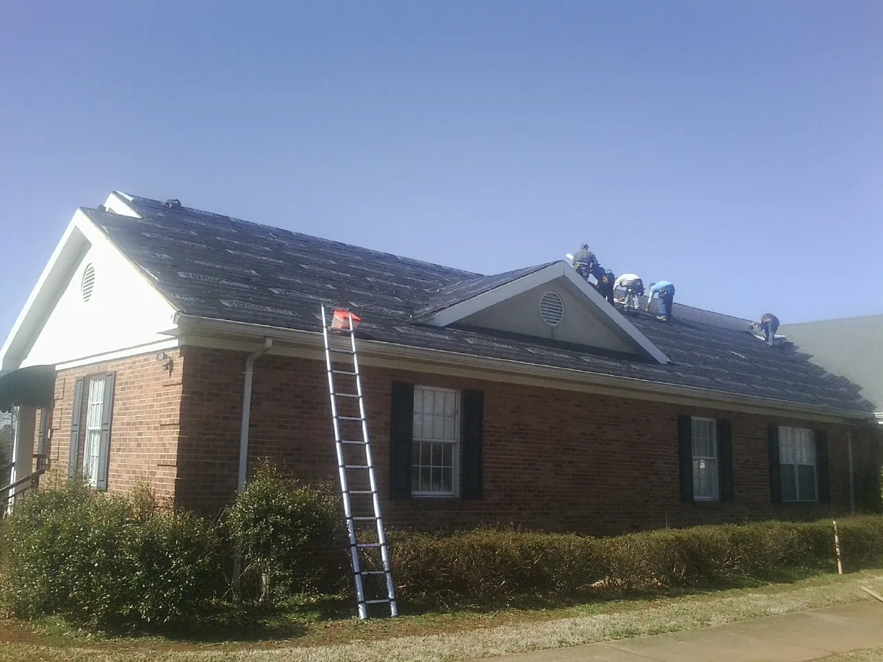 Crew tearing shingles off a brick ranch roof with a ladder set — Metal Roof Repair work by our crew in Lefor