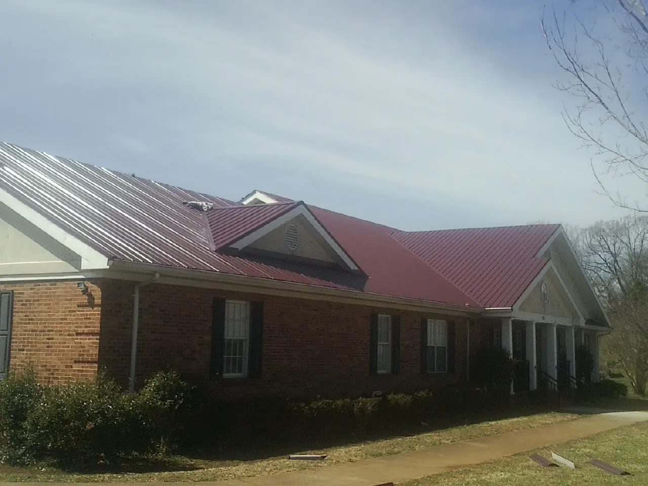Red metal roof with gabled entries on a long brick building, from a Hail Damage Roof Repair job in Lefor