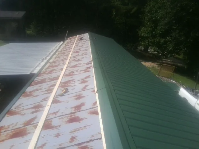 Old rusted panels beside newly installed green metal roofing — Wind Damage Roof Repair by Roofing Brothers in Lefor