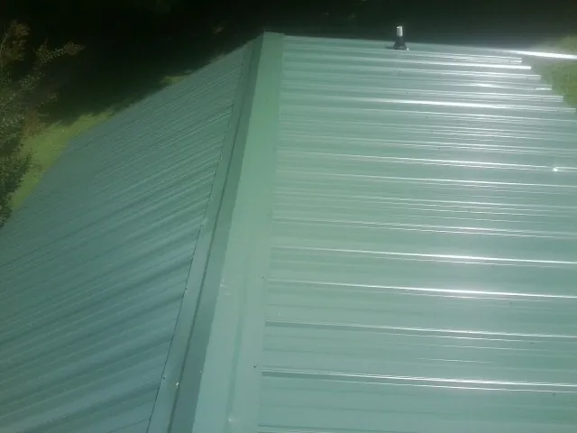 New green metal panels meeting at the ridge of a roof — Flat Roof Repair work by our crew in Lefor