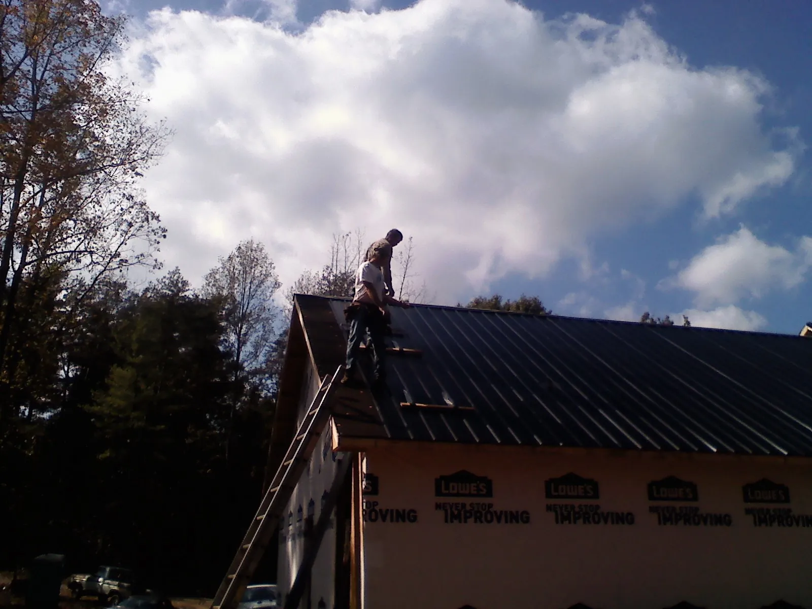 Roofer fastening dark metal panels high against a cloudy sky, from a Roof Inspection job in Lefor