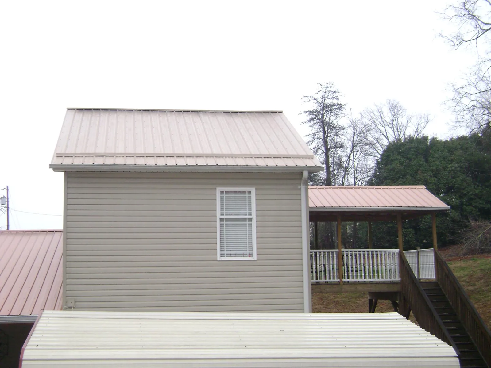 Tan metal roofs on a two story addition and attached porch, from a Roof Replacement job in Lefor